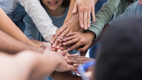 The group of multi racial unrecognizeable people put their hands in together signifying their unity.