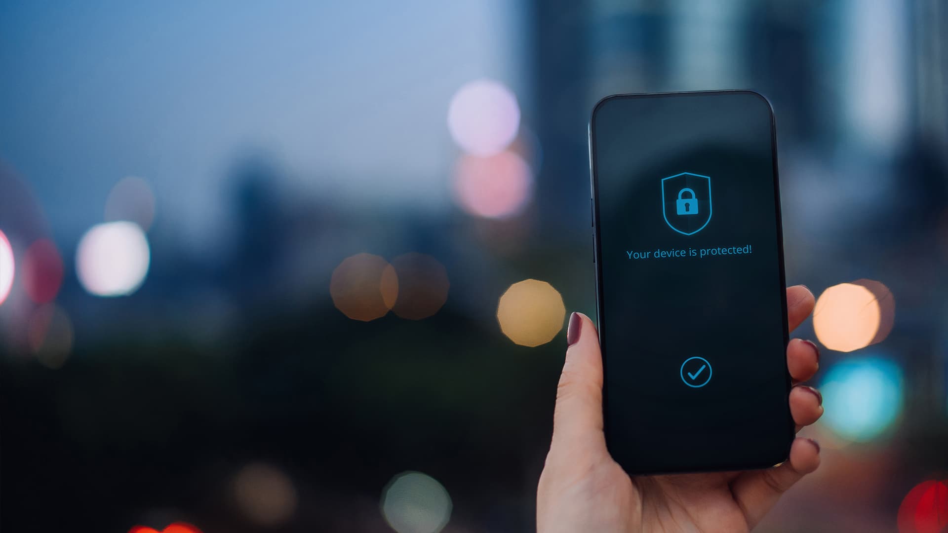 Close up of female hand holding up smartphone against illuminated cityscape in the city, with security key lock icon on the device screen. Privacy protection, internet and mobile security concept