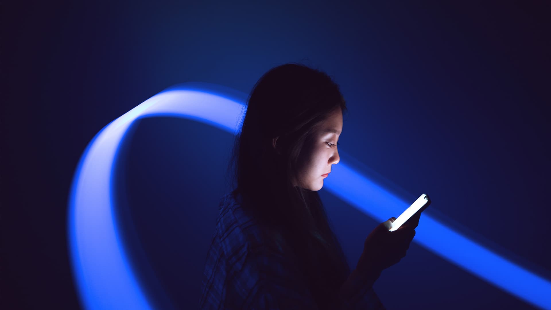 A woman looking at her phone in a dark room lit up by blue lights.