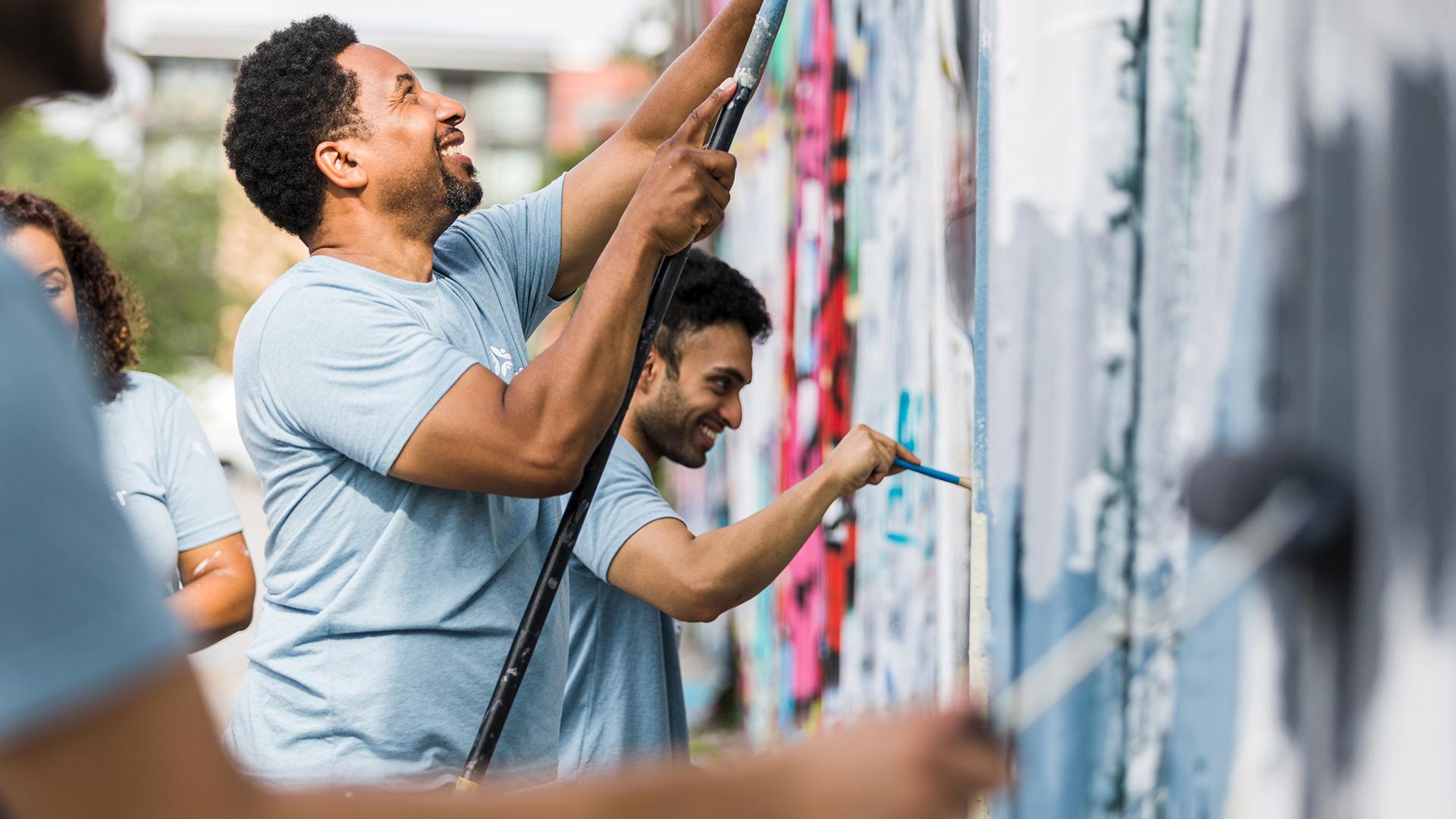 The group of coworkers smile while they help paint the graffiti wall.