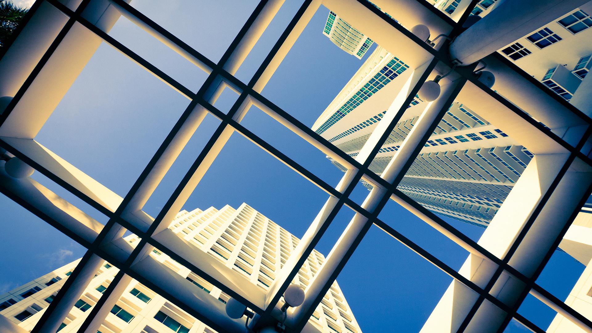 Looking up at a cluster of skyscrapers converging into a blue sky with clouds.