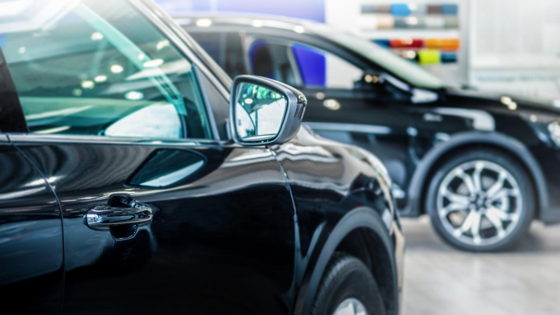 Shiny, black cars parked inside an indoor car sales lot.