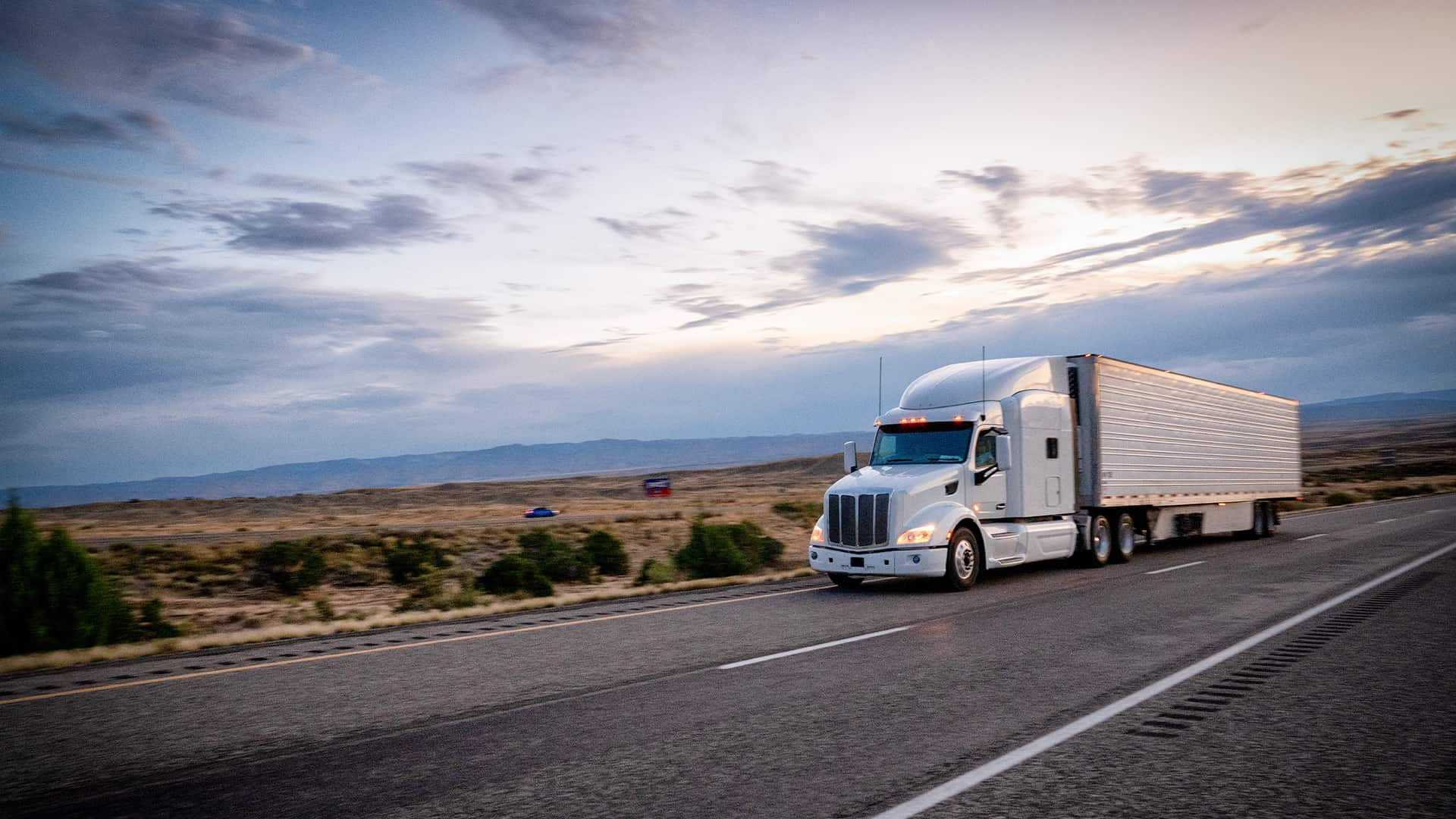 A truck driving down a remote desert highway.