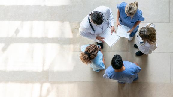 A group of healthcare professionals standing in a circle discussing a patients chart.