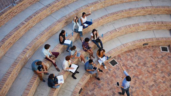 Students having class with book and tablets, in outside auditorium. Students with raised hands