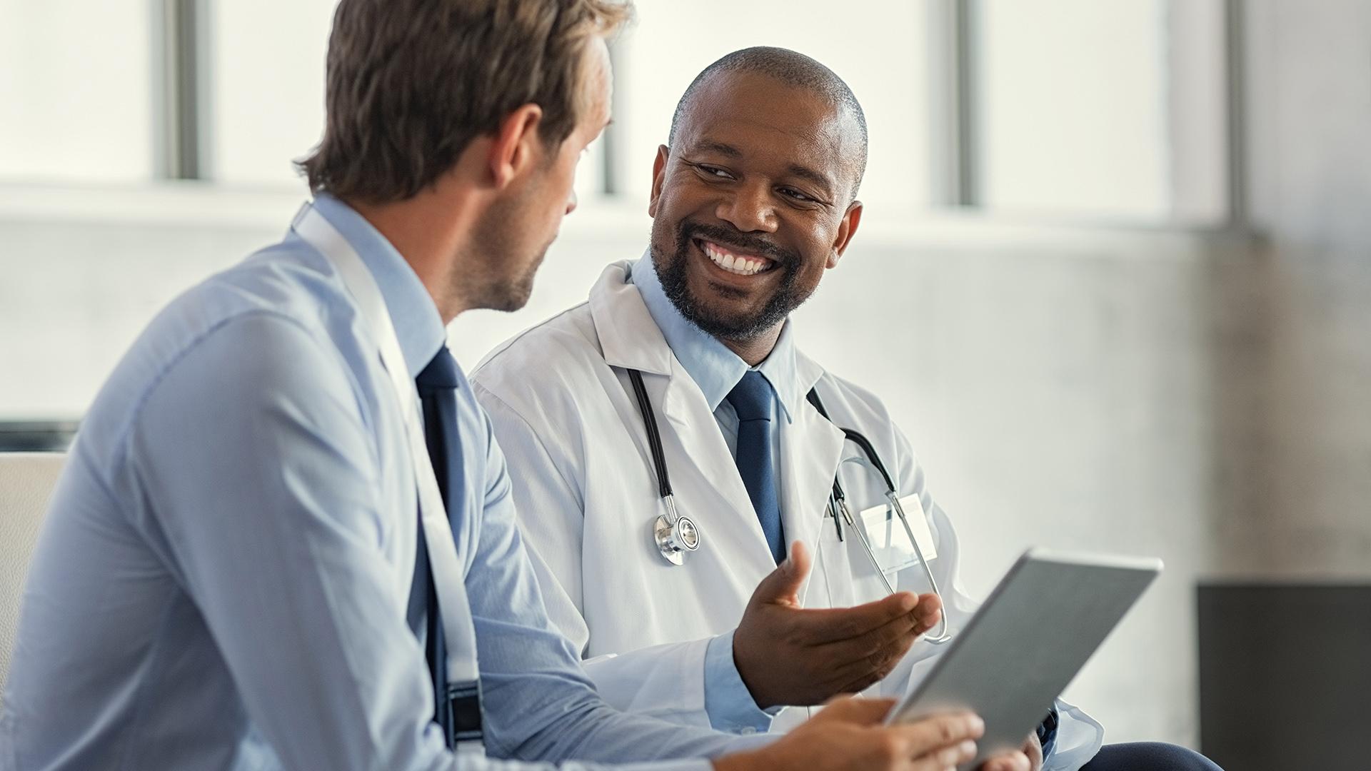 Two mature smiling doctors having discussion about patient diagnosis, holding digital tablet.