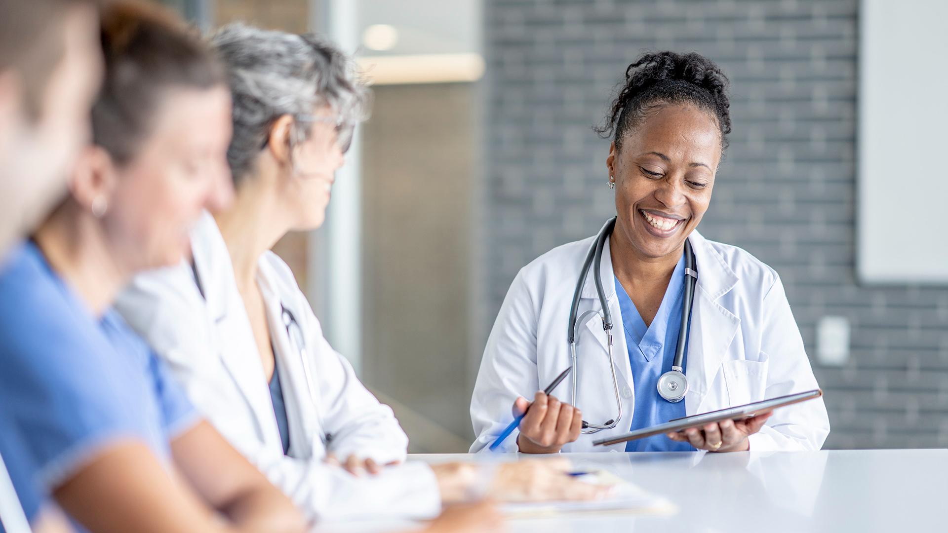 A small group of medical professionals sit around a boardroom table as they meet to discuss their patients needs. 