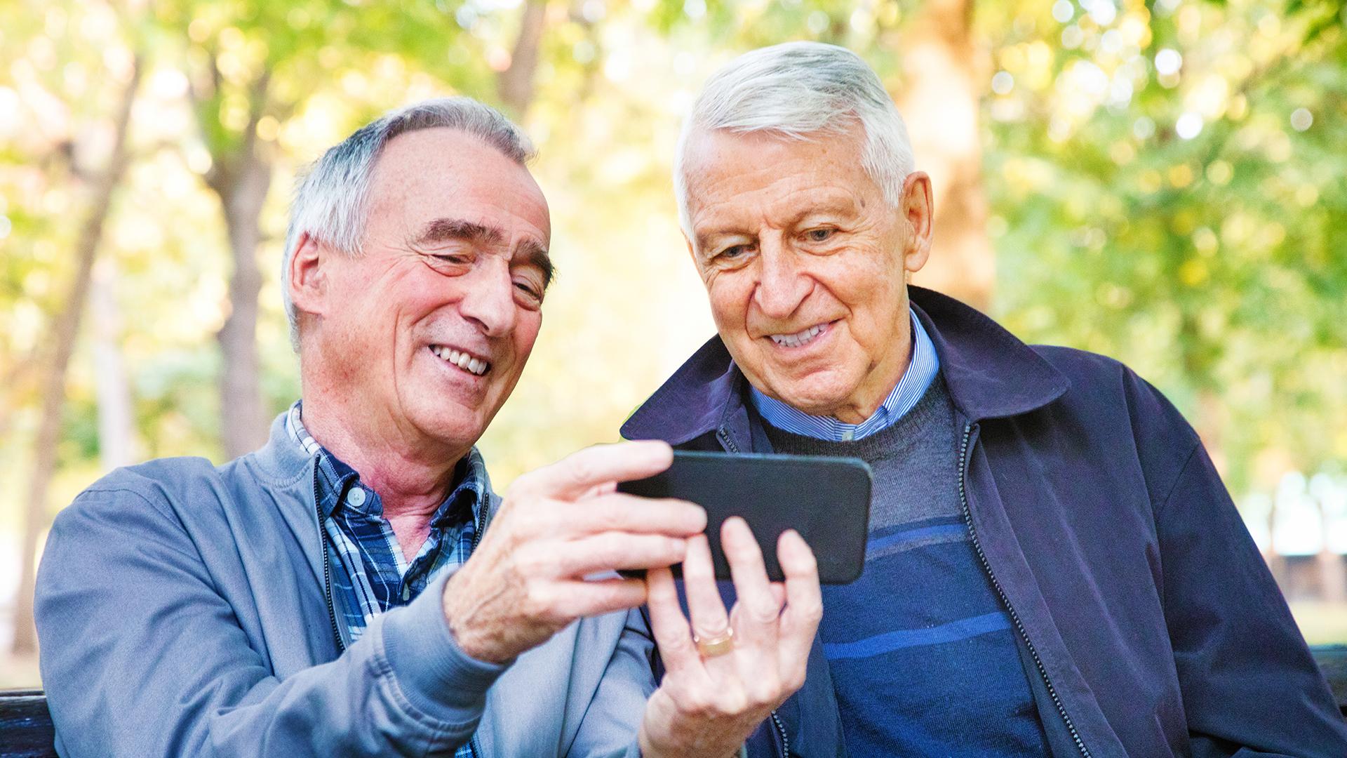 Two senior men enjoying medi aon mobile phone together in park