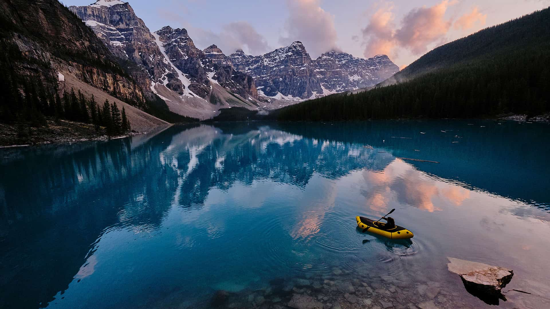 Young woman kayaks across mountain lake at sunrise