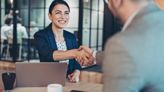 Two business people shaking hands in a modern office setting.