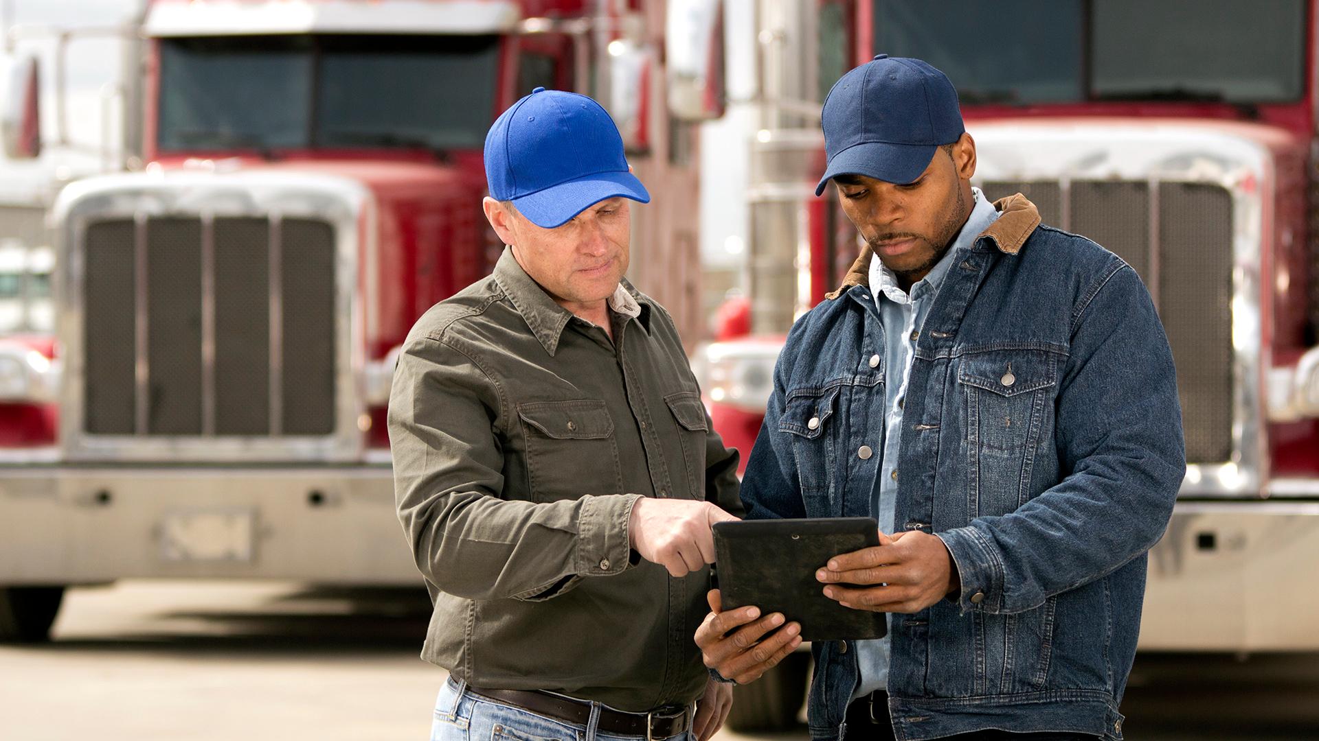 Two semi truck drivers looking at notes on an iPad.