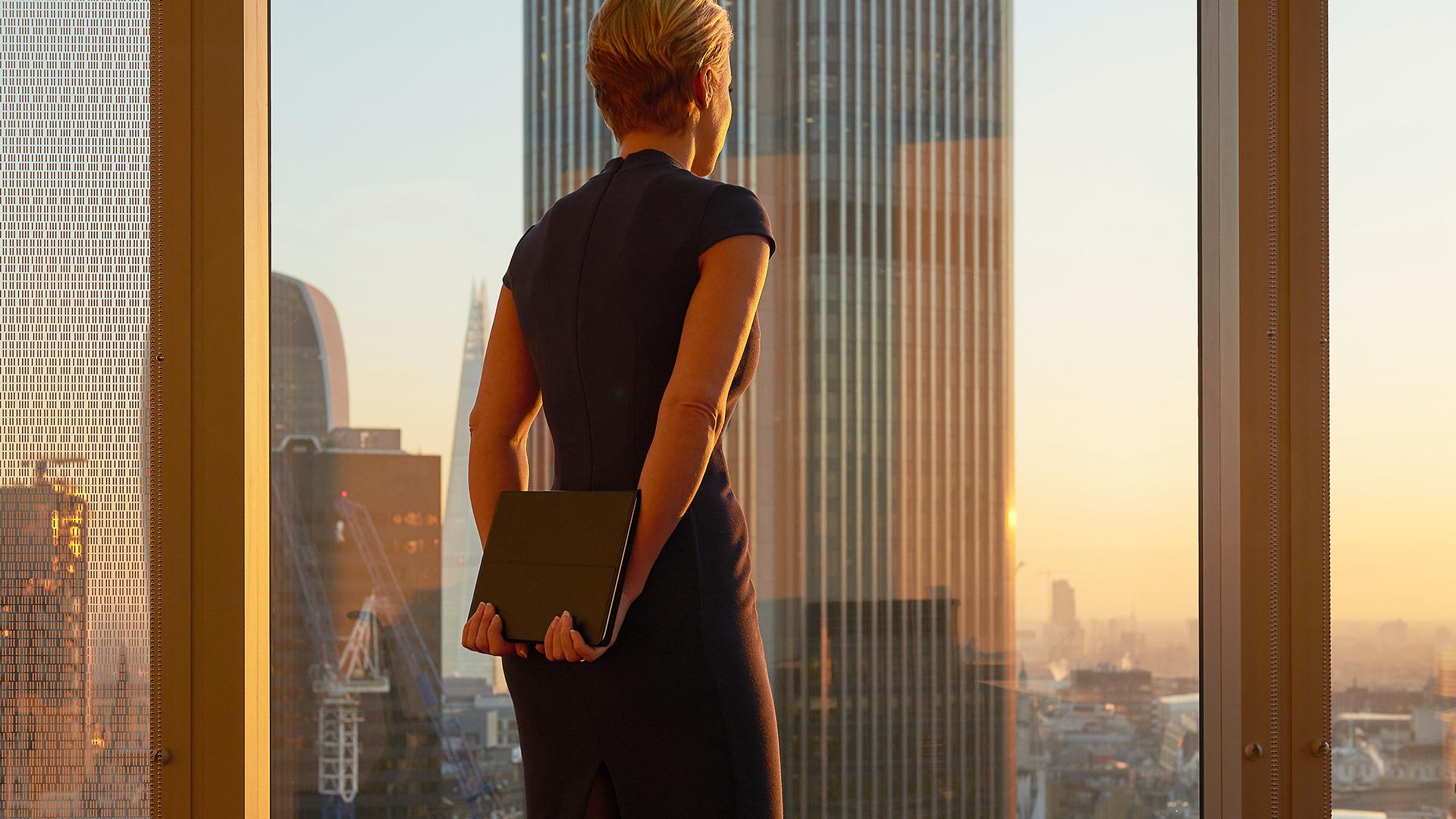 Business woman looking longingly out a high rise office window.
