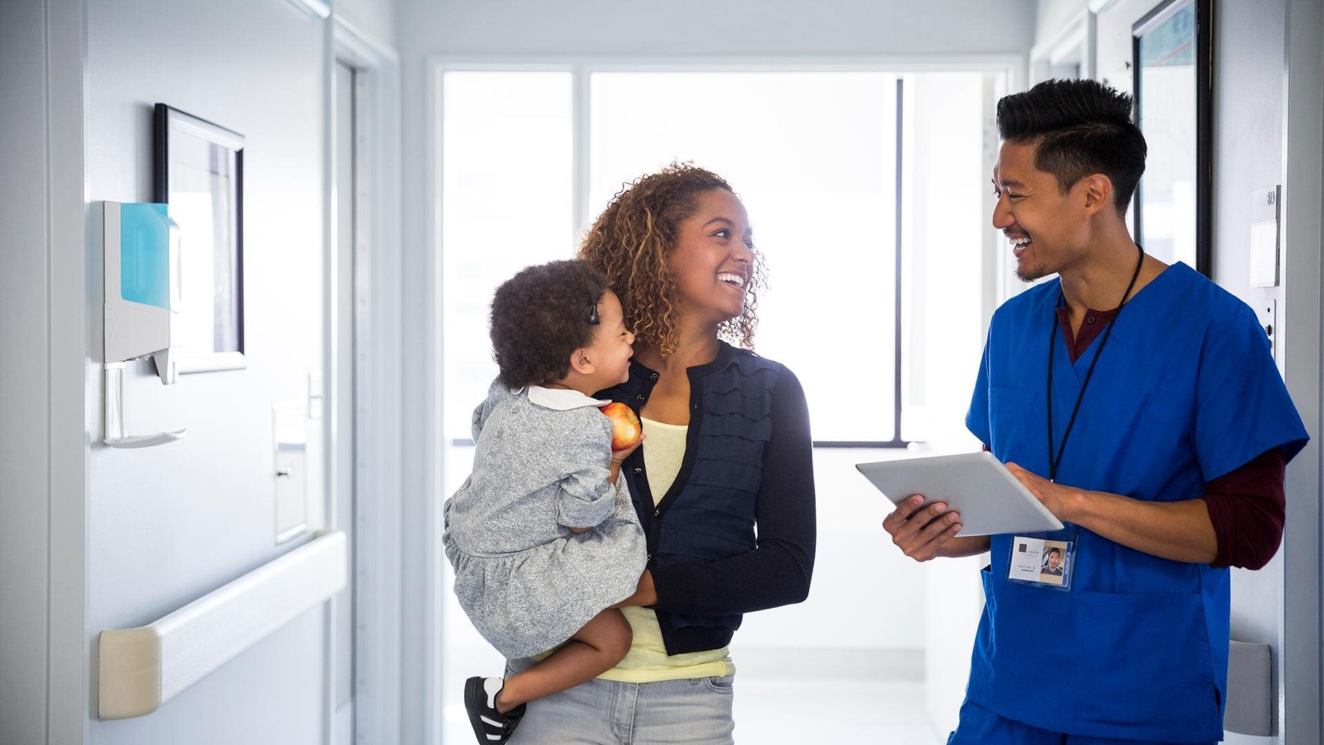 A physician smiling at his young patient and his mother.