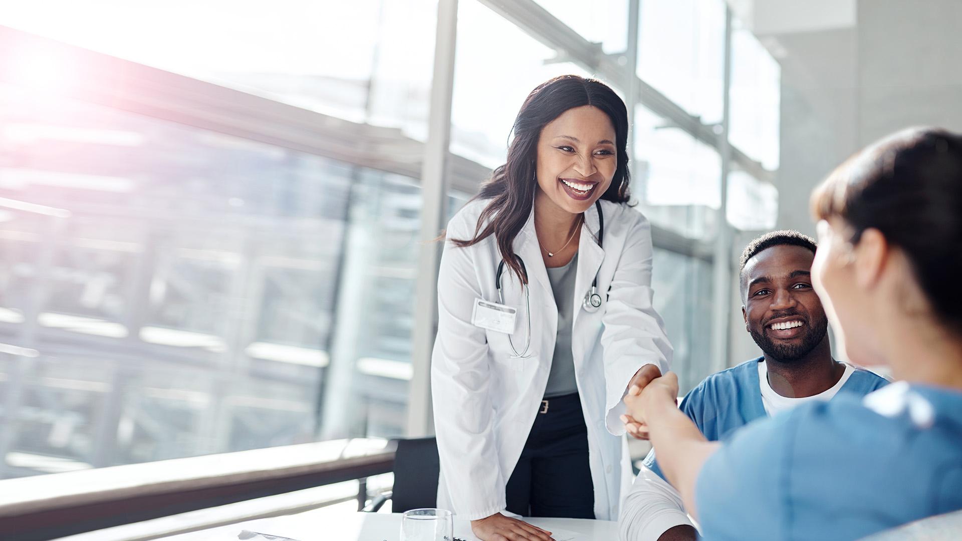 A woman doctor smiles and shakes hands with a student nurse.