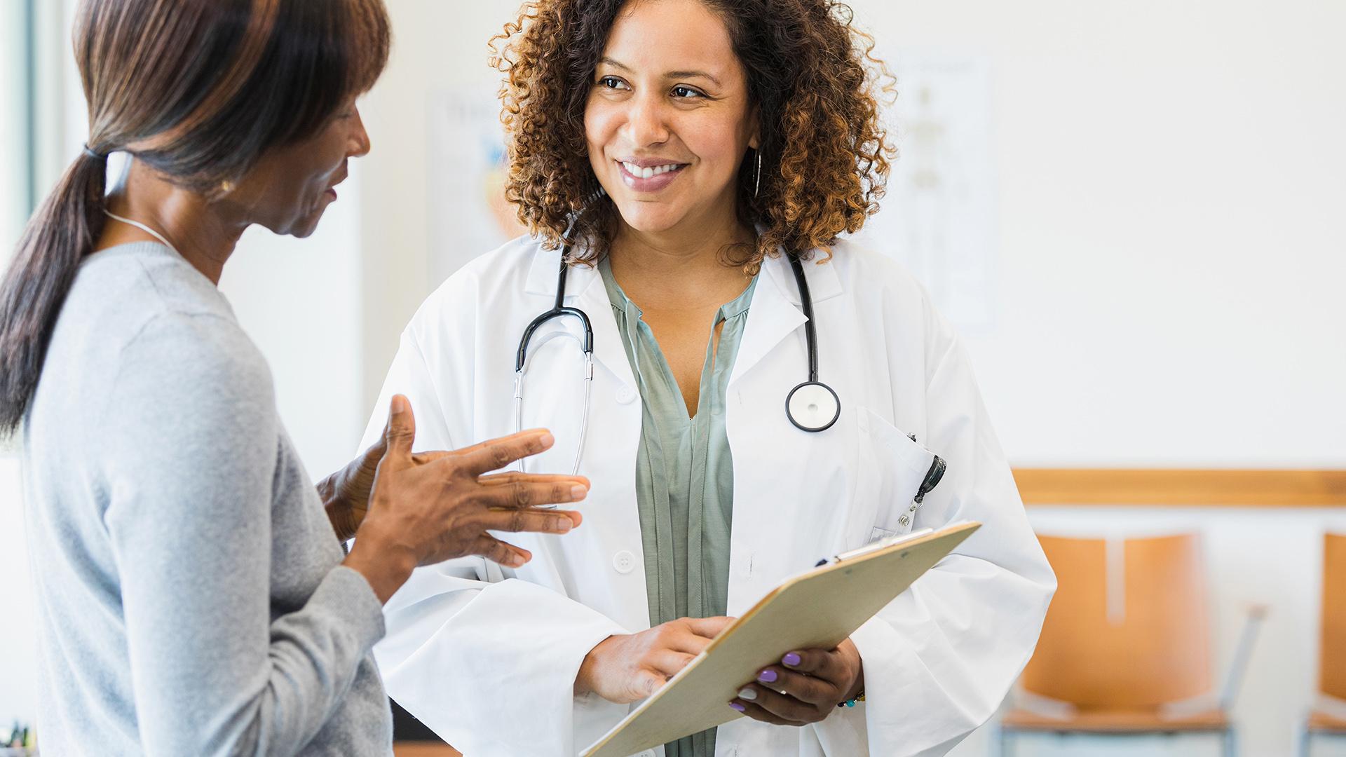 Doctor smiles as patient asks questions about information on clipboard