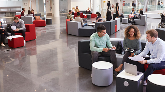 Employees sitting in university atrium, three in foreground