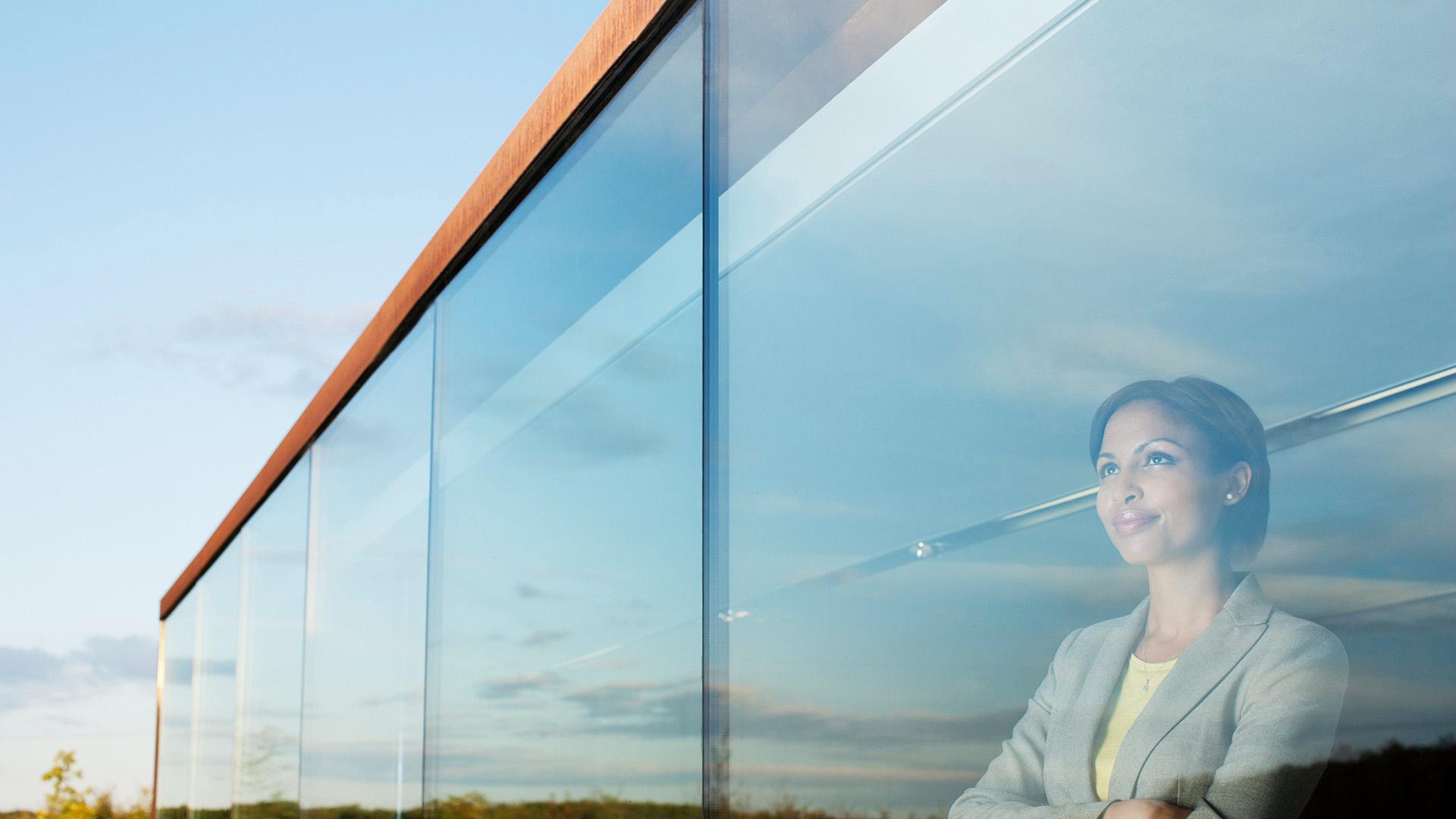 A woman smiling while she looks out the window of a high rise office building.