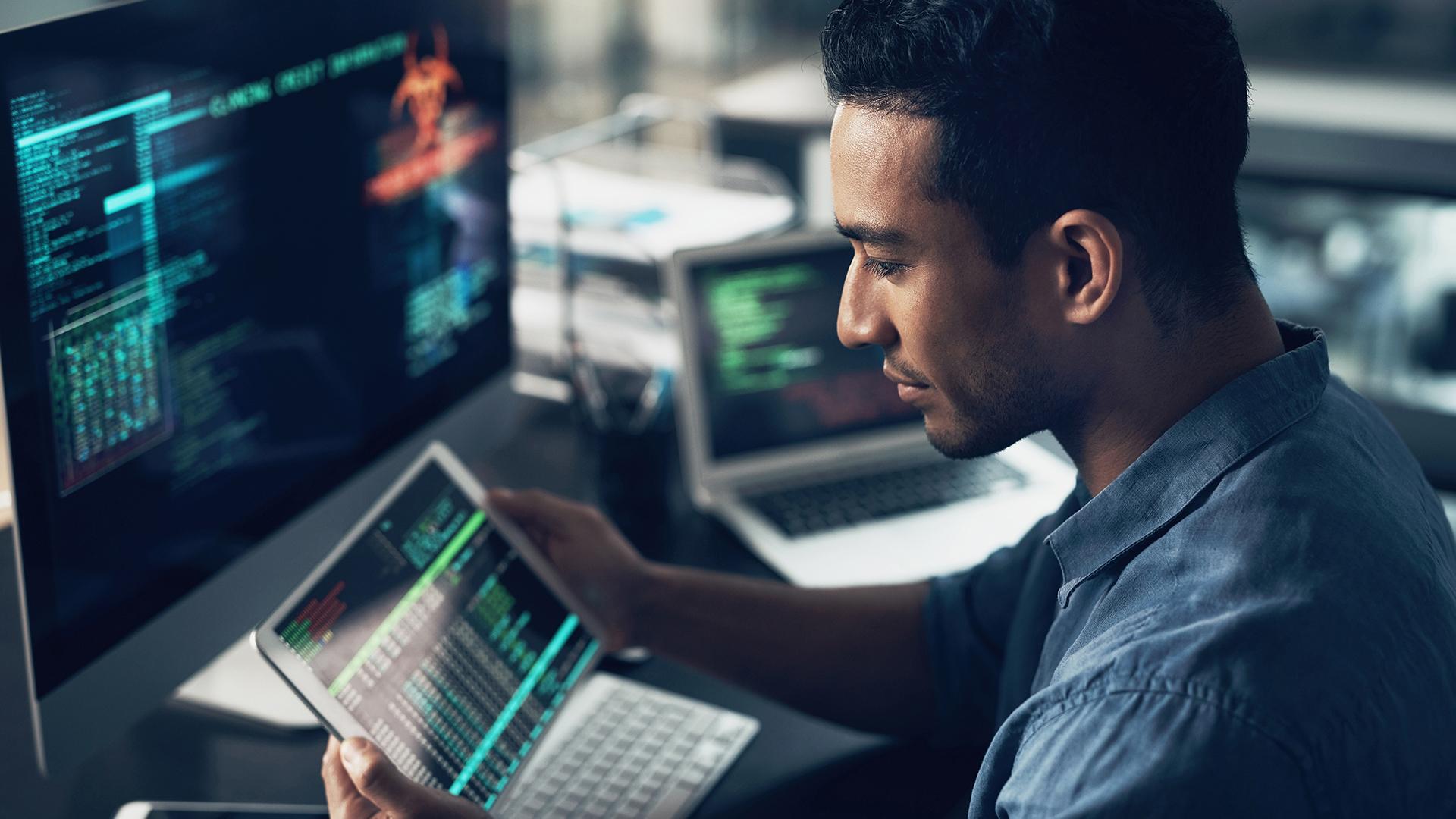 Shot of a young man using his digital tablet and computer in a modern office