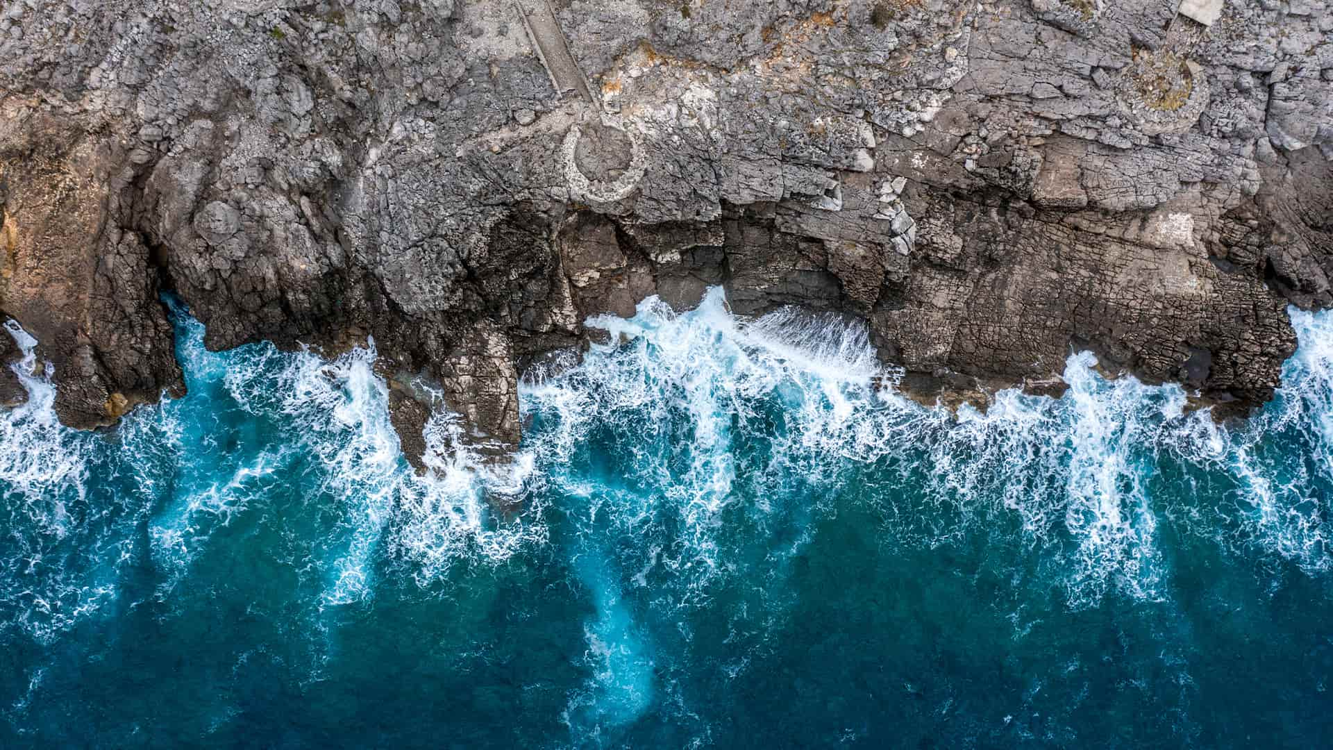 A view directly above a steep rocky shoreline coming out of the sea