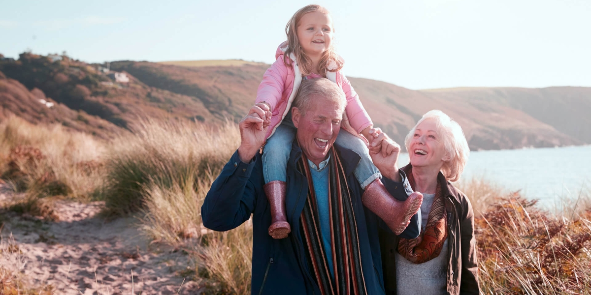 Grandparents walking on beach with granddaughter on shoulders