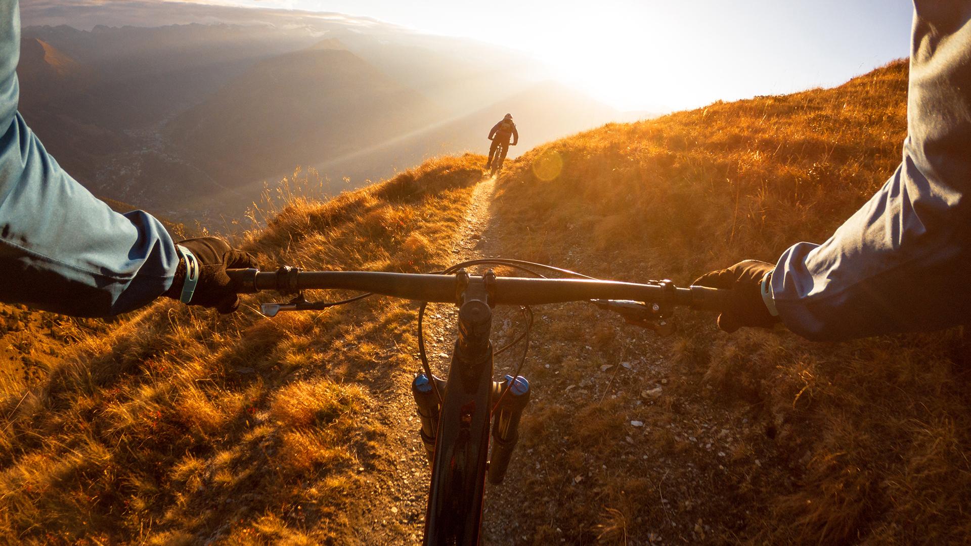 Personal perspective shot of a man mountain biking with a friend in the Alps