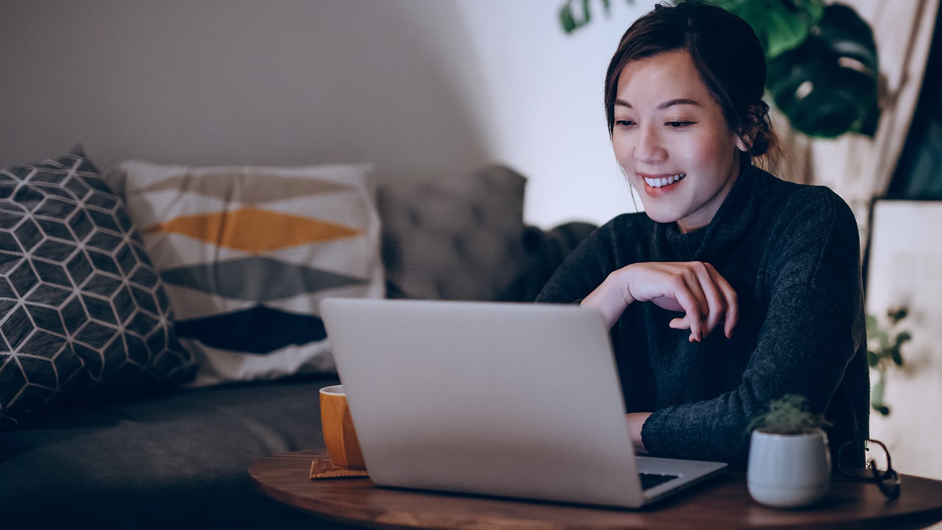 A woman sitting at her desk on her laptop, smiling at the screen.