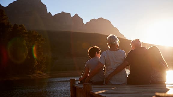 Grandchildren With Grandparents Sitting On Wooden Jetty