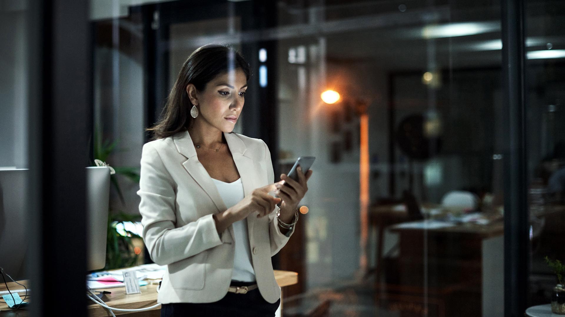 A business woman checking her smart phone late at night.