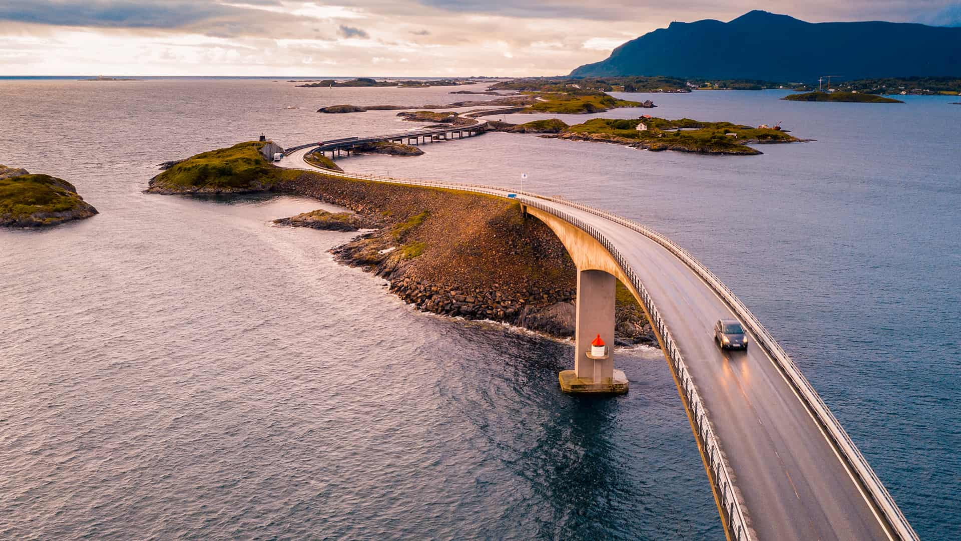 Aerial view of a car driving down a highway that stretches over the ocean.