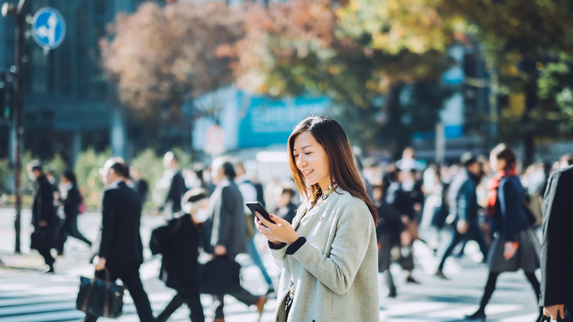 Young smiling lady using smartphone outdoors in busy downtown city street