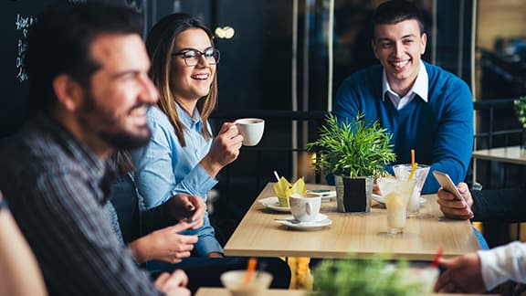 People sitting around a table in a cafe, smiling and drinking coffee.