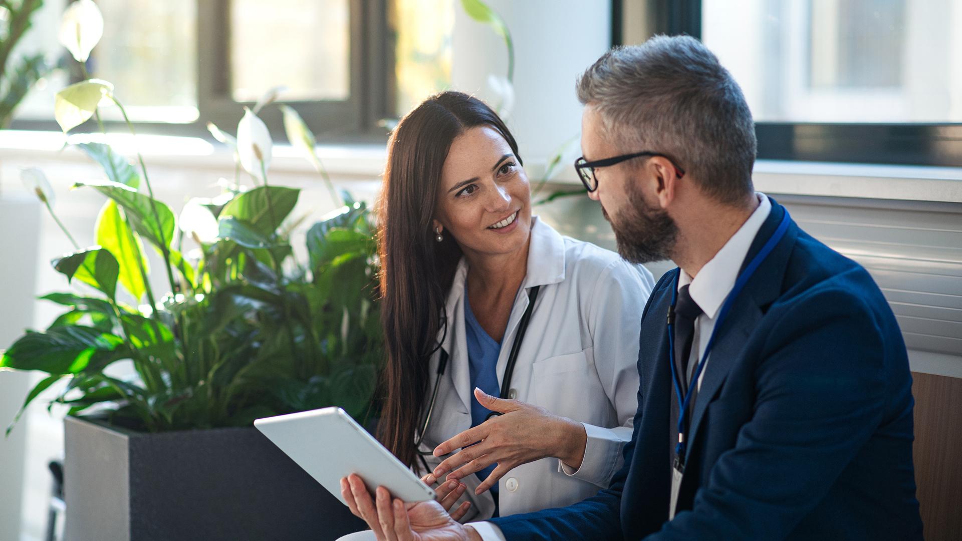 Businessman showing something in digital tablet to doctor in hospital corridor