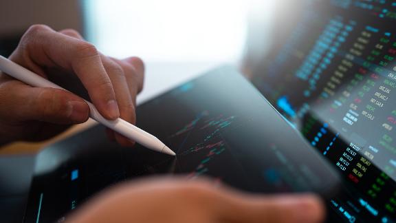 A business person tracking the technical movement of a stock chart on a computer screen.