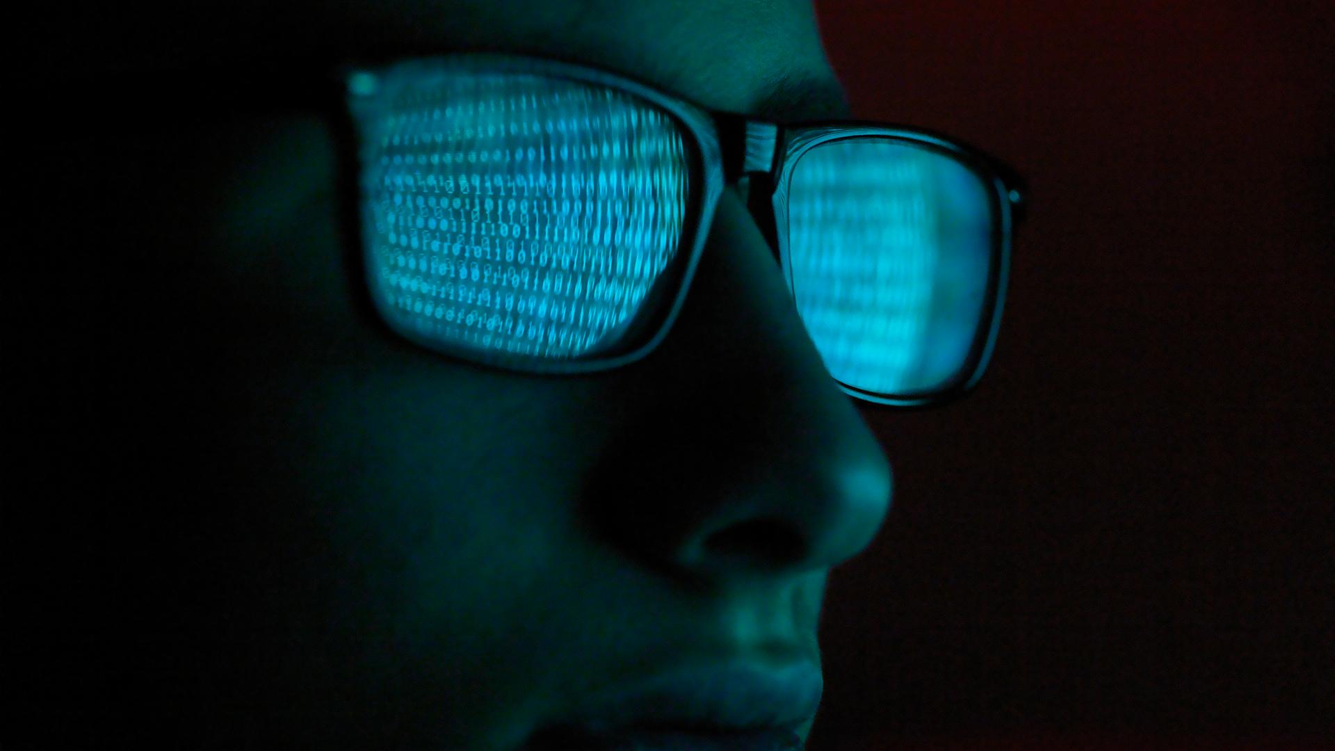 Close up of a person wearing glasses, with a computer screen reflected in lenses.