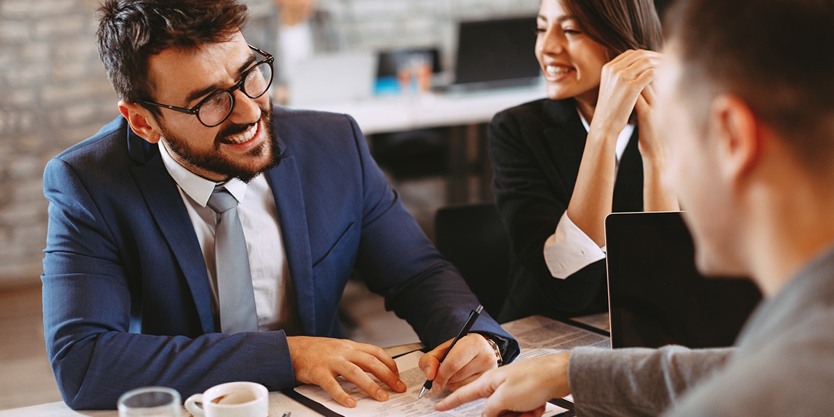 Smiling man signs paperwork where another man points